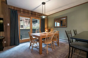 Uma sala de jantar com mesa e cadeiras de madeira, um lustre e uma porta de vidro deslizante que dá para uma varanda.