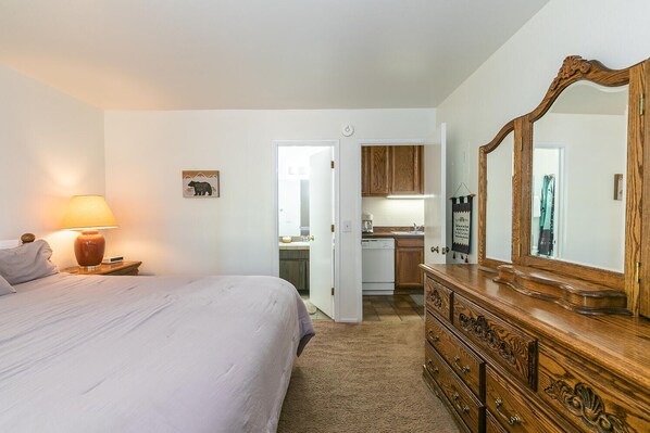 A bedroom with a bed, a bedside lamp, a dresser, and a mirror.