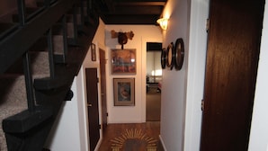 Un couloir doté d’un plancher en bois, d’un escalier et d’une porte donnant sur une autre pièce.