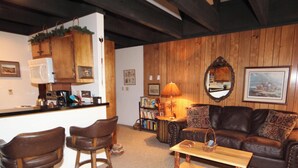 Un salon chaleureux avec un canapé en cuir, des murs en bois, un coin café et une bibliothèque.
