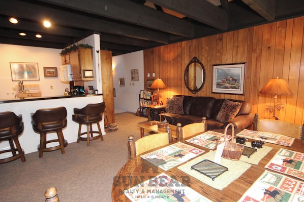 A cozy living room with a wooden ceiling, a bar area, and a seating arrangement including a sofa and chairs.