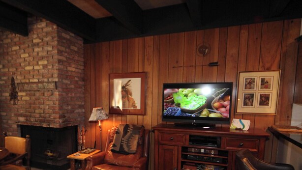 Un salon chaleureux avec une cheminée en briques, des murs en bois, un téléviseur et des tableaux encadrés.