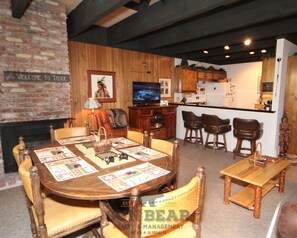 A dining area with a wooden table and chairs, a television, and a kitchen in the background. - Lakefront Condo Complex / Beach Access (LA999 18) (Incline Village)