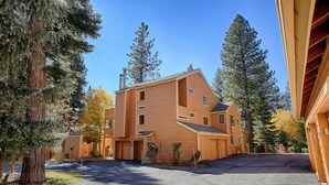 A multi-story building with a sloped roof, surrounded by tall trees and a clear sky. - Condo at the popular McCloud complex (MC255) (Incline Village)