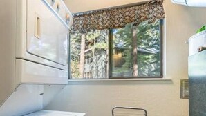 A compact kitchen with a window overlooking a forest, a small table, and a cabinet. - Beautiful Golf Course Views! (PE865-4) (Incline Village)