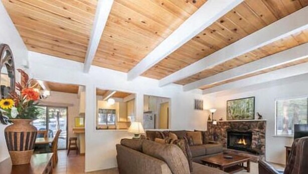 A cozy living room with a fireplace, wooden beams, and a dining area with a vase of flowers. - Beautiful Golf Course Views! (PE865-4) (Incline Village)