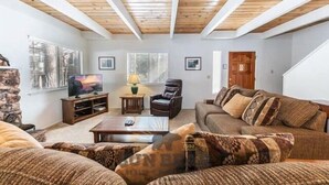 A living room with a wooden ceiling, a sofa set, a television, and framed pictures on the wall. - Beautiful Golf Course Views! (PE865-4) (Incline Village)