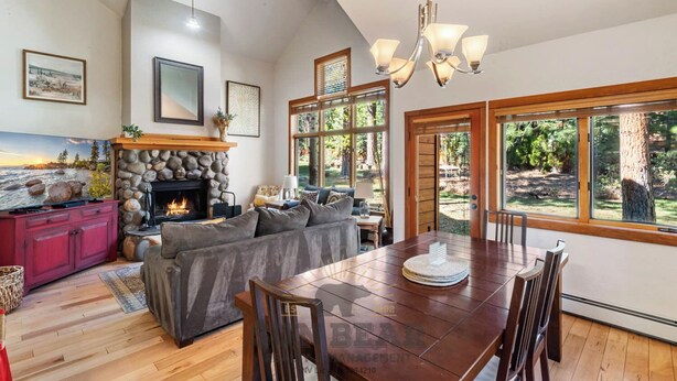 A spacious living room with a fireplace, a dining area, and large windows offering a view of the outdoors.