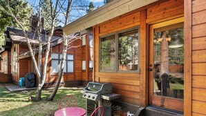 A wooden cabin with a grill, two red chairs, and a small table.
