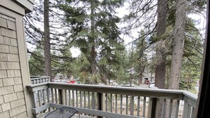 A wooden deck with metal chairs and a railing, overlooking a residential area with trees and parked cars. - Cozy Condo in Incline (IM62) (Incline Village)