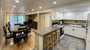 A compact kitchen with a dining area, wooden stools, a stove, and white cabinets. - Cozy Condo in Incline (IM62) (Incline Village)