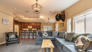 A living room with a sectional sofa, a wooden coffee table, a leather armchair, a kitchen area with wooden cabinets, and a mounted buffalo head. - Newly remodel and spacious home (830SO) (Incline Village)