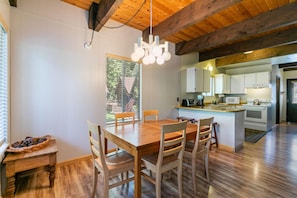 A modern kitchen with white cabinets, a wooden dining table, and a hanging light fixture.