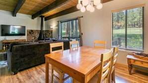Een gezellige woonkamer met een houten plafond, een stenen open haard, een grote televisie en een eethoek met een houten tafel en stoelen.