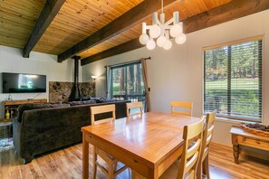 A cozy living room with a wooden ceiling, a stone fireplace, a large TV, and a dining area with a wooden table and chairs.