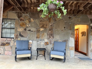Eine Terrasse mit Steinwänden, zwei Korbstühlen und einem kleinen Tisch.