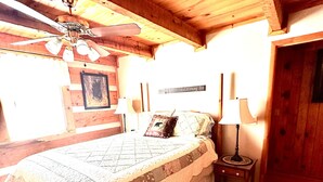 Ein Schlafzimmer aus Holz mit Bett, Nachttisch, Lampe und Deckenventilator.