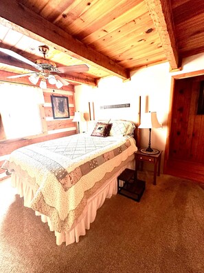 A wooden bedroom with a bed, a nightstand, a lamp, and a ceiling fan. - Bruno's Mountain Cave 3 Bedroom Cabin by RedAwning (Sevierville)