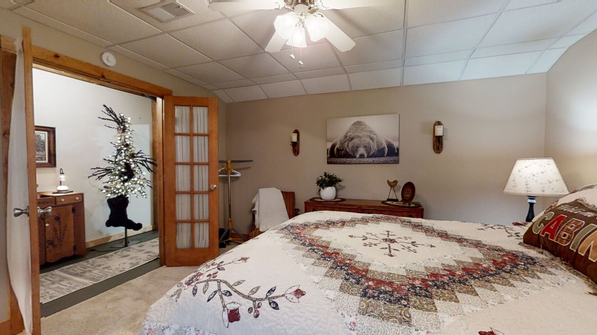 Une chambre à coucher avec un grand lit, un ventilateur de plafond, une porte, une petite table, une lampe et un tableau accroché au mur.