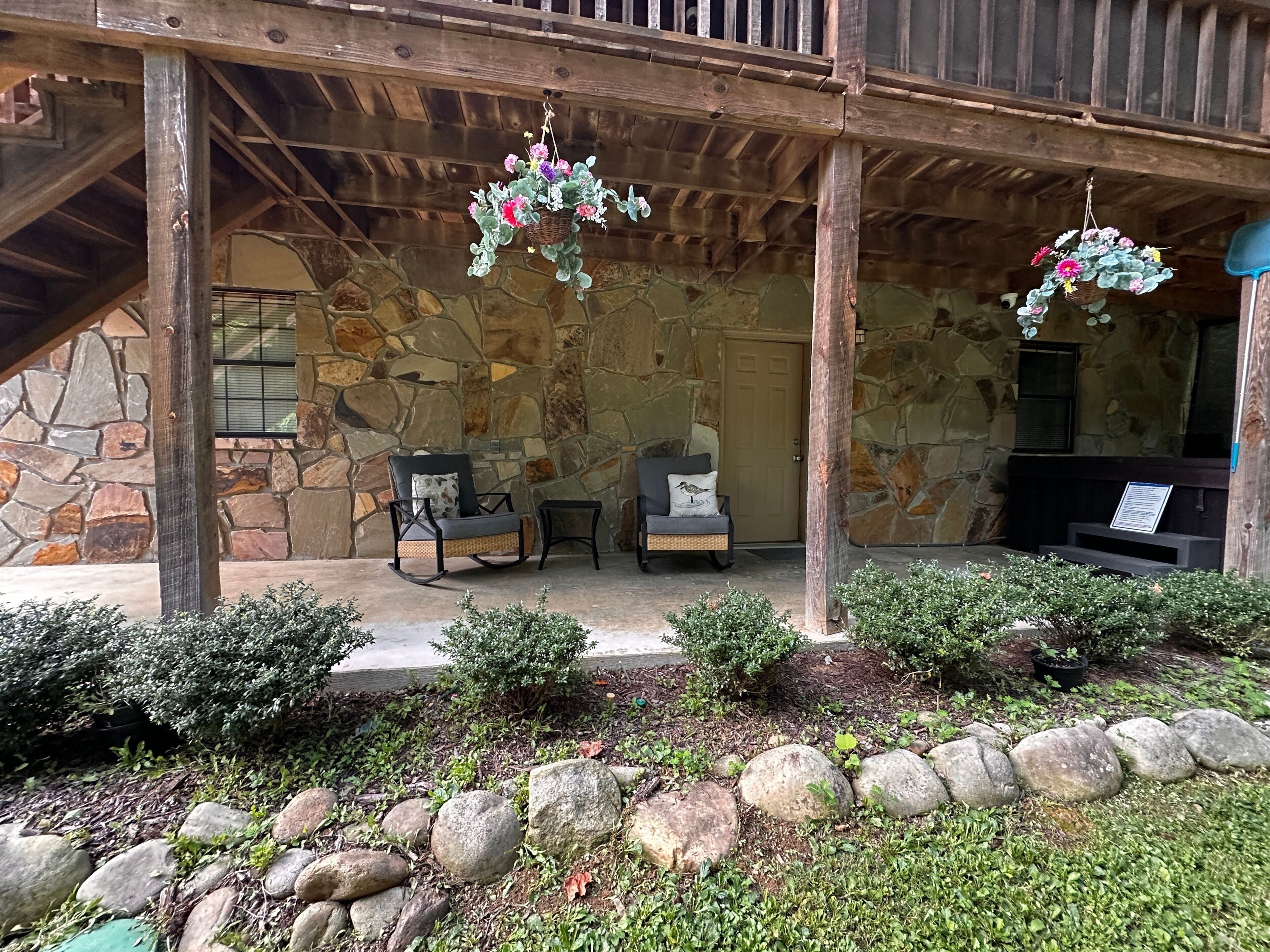A stone exterior with a wooden porch, two rocking chairs, and hanging flower baskets.