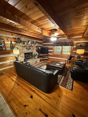 A log cabin interior with a fireplace, leather sofas, and a television. - Bruno's Mountain Cave 3 Bedroom Cabin by RedAwning (Sevierville)