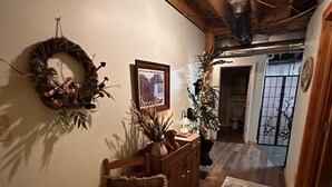 A hallway with a wooden ceiling, a wreath on the wall, a framed picture, a Christmas tree, and a patterned rug.