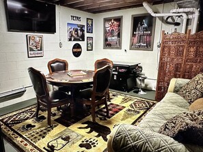 Ein Zimmer mit einem runden Tisch, vier Stühlen, einer Couch und Postern an der Wand.