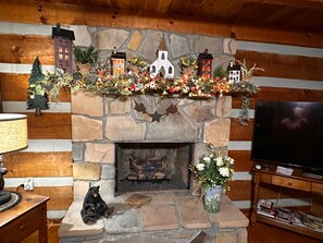 A stone fireplace with a mantel decorated with various items, a television on a stand to the right, and a bear figurine on the mantel. - Bruno's Mountain Cave 3 Bedroom Cabin by RedAwning (Sevierville)