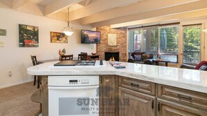 A kitchen with a built-in stove, a dining area with chairs, a fireplace, and a large window with blinds. - Lakefront Condo Complex - Beach Access (LA999 35) (Incline Village)