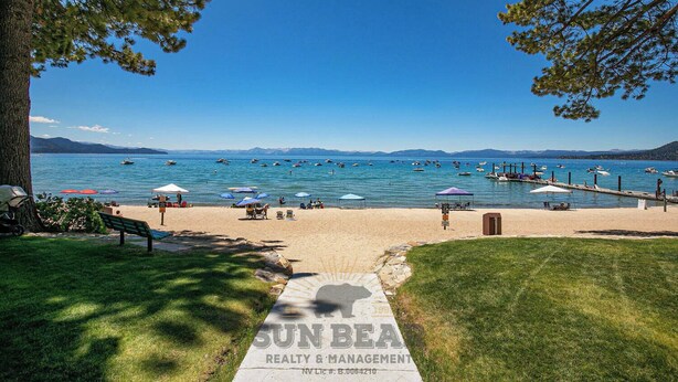 A beach with a clear view of the water, umbrellas, and a pathway leading to the beach. - Lakefront Condo Complex - Beach Access (LA999 35) (Incline Village)