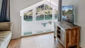 Une pièce comprenant un meuble en bois, un canapé et une fenêtre donnant sur un plan d’eau et de la verdure.