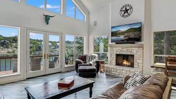 A spacious living room with a fireplace, large windows, and a view of the outdoors.