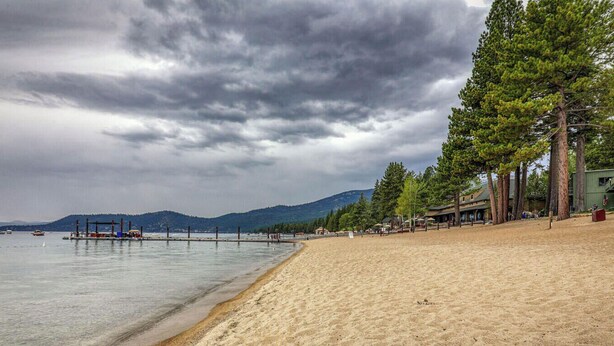 Ein Strand mit einer Seebrücke, Bäumen und einer Bergkulisse.