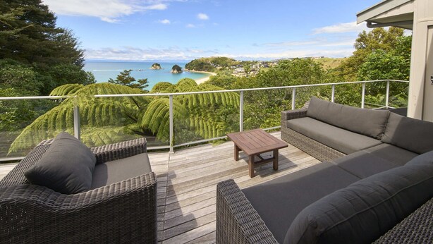 Eine Terrasse mit Korbmöbeln, einem kleinen Tisch und Blick auf Strand und Wald.