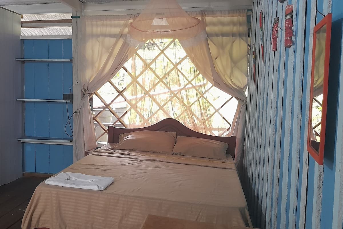 A small, cozy room with a single bed, a blue wardrobe, and a window with a decorative curtain.