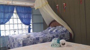 A bedroom with a bed, a window with blue curtains, a canopy, and a wall with decorative items. - Hostal Ebenezer Macedonia Tikuna (Leticia)