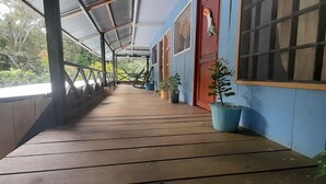 A covered wooden deck with potted plants, a metal railing, and a view of greenery. - Hostal Ebenezer Macedonia Tikuna (Leticia)