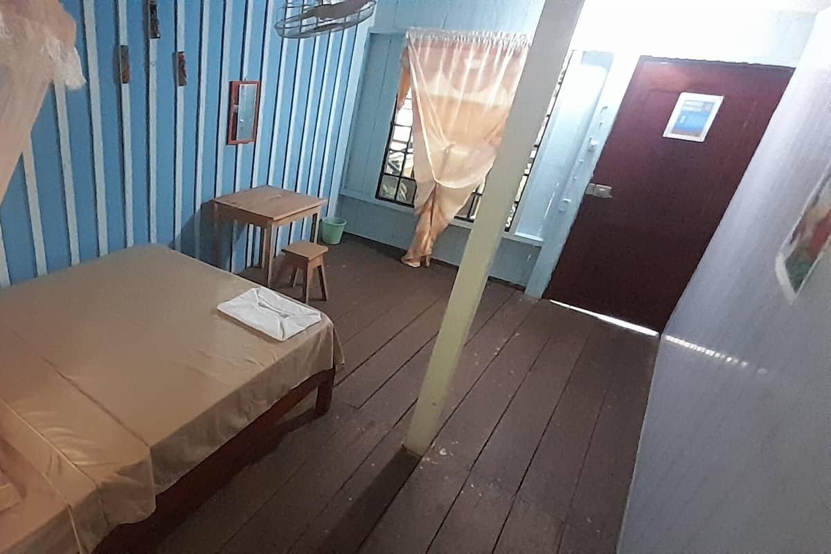A room with a bed, a small table, a chair, a window with a curtain, and a door.
