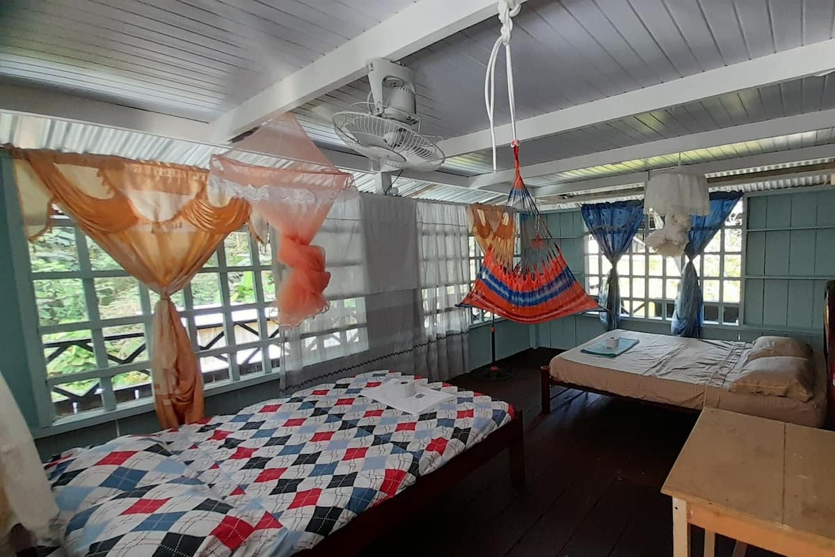 A room with two beds, a wooden table, and a hammock.