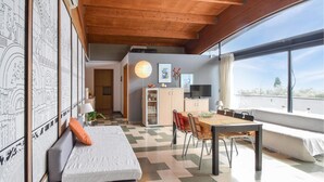 Une pièce chaleureuse avec un plafond en bois, un coin repas avec une table et des chaises, une cuisine équipée de placards et d’un téléviseur, et une grande fenêtre offrant une vue dégagée.
