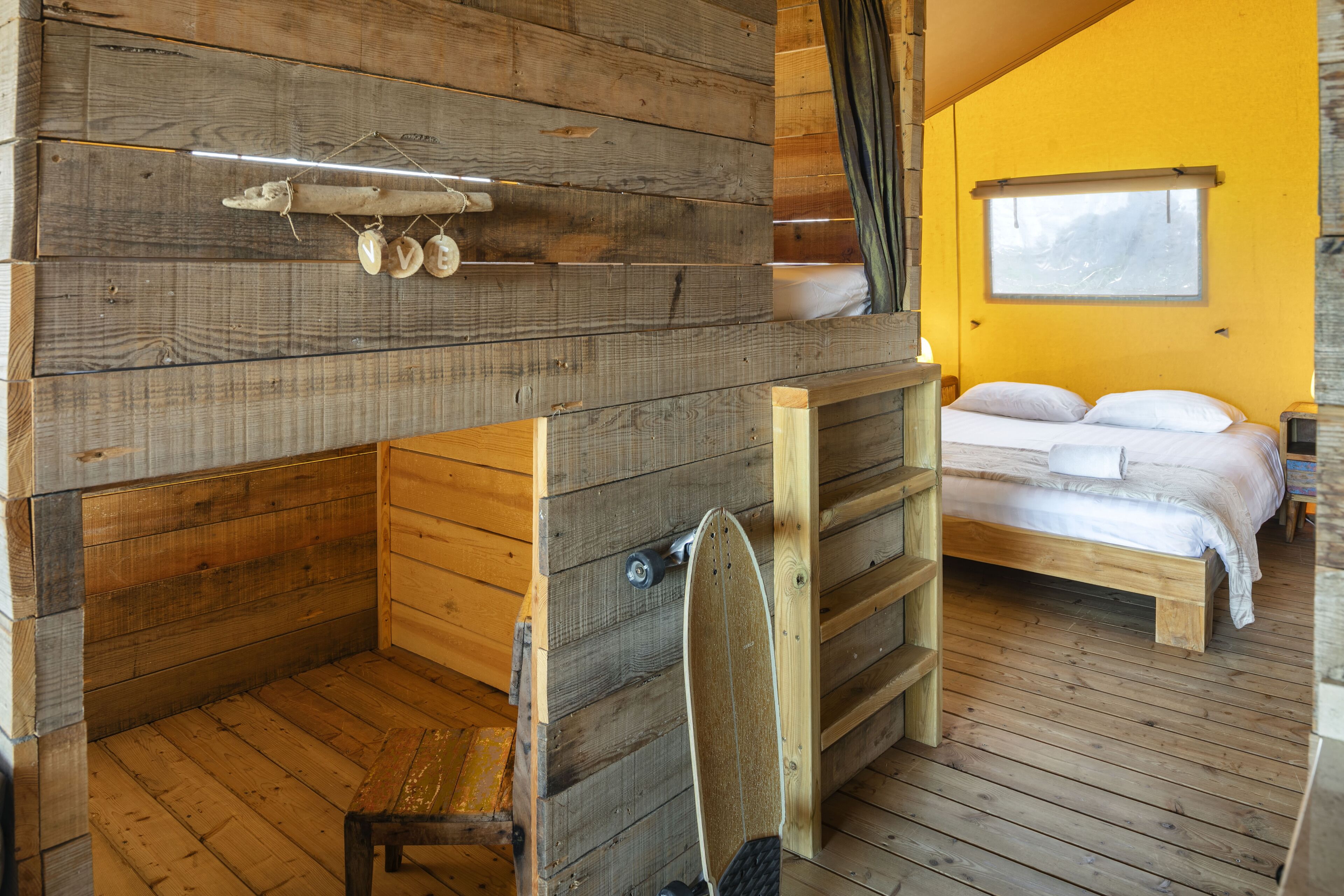 Un interior de madera con una litera, un estante con conchas marinas y una ventana con vistas.