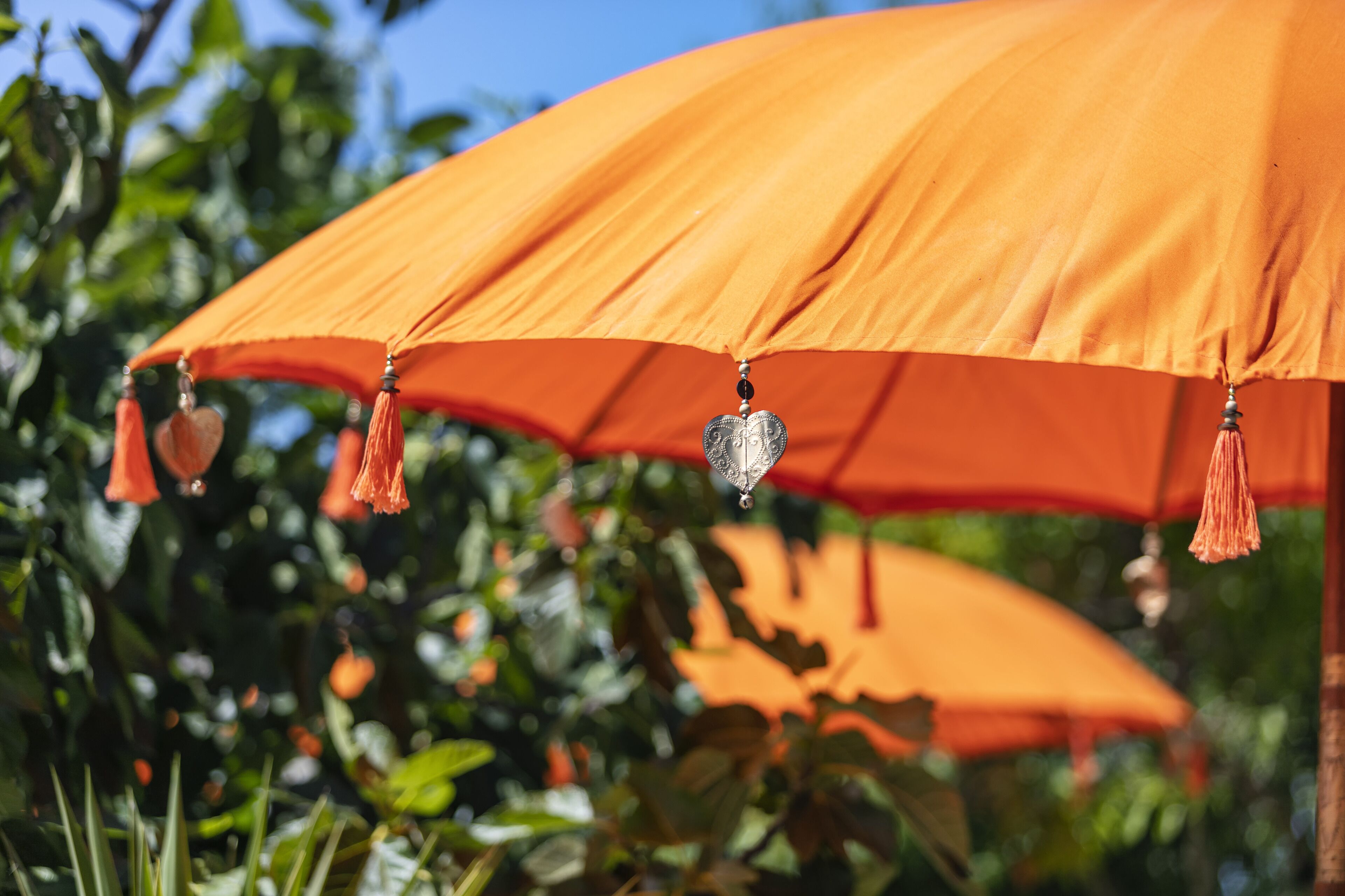 Un gros plan d’un parapluie orange orné de glands et d’un pendentif en forme de cœur.
