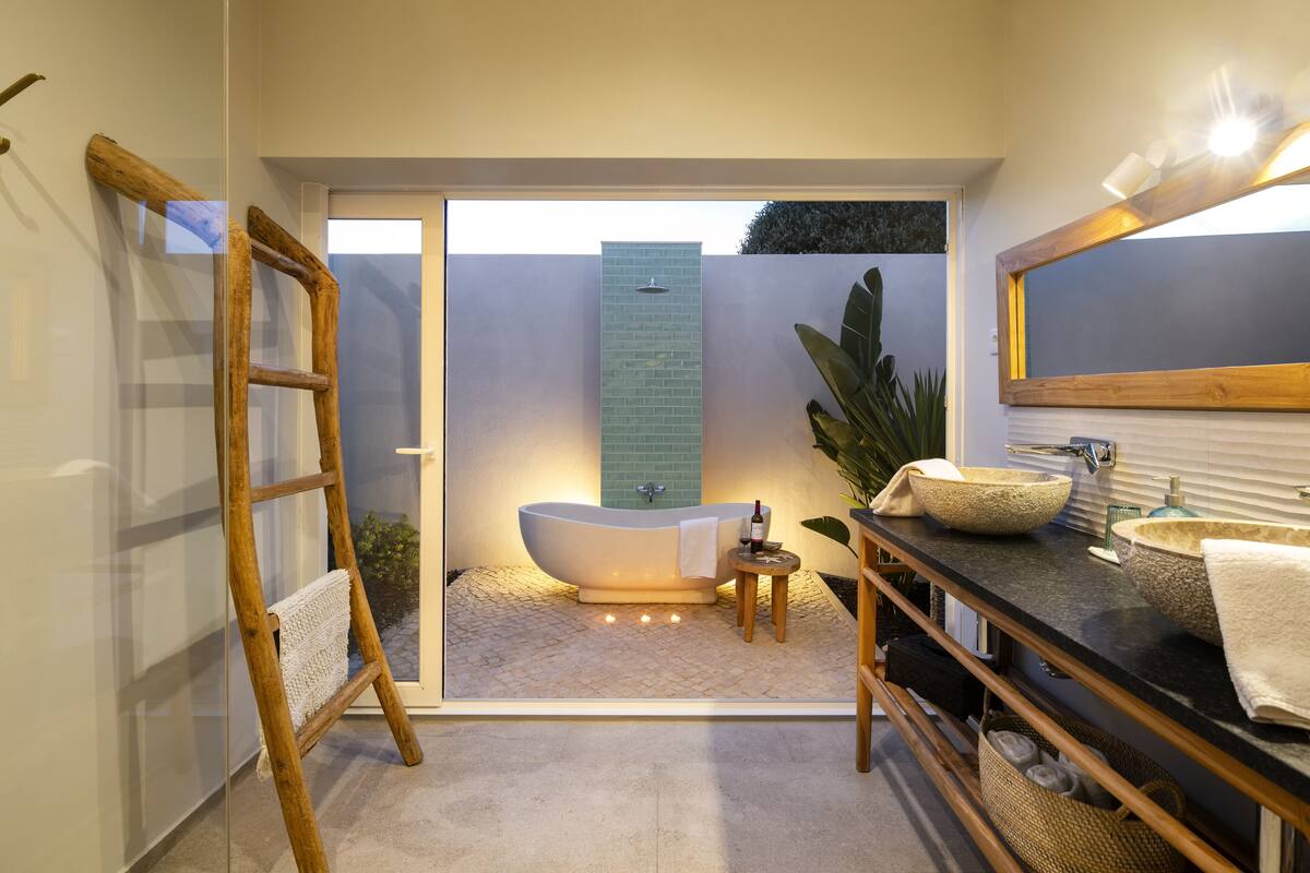 A modern bathroom with a freestanding bathtub, a large mirror, and a wooden ladder.