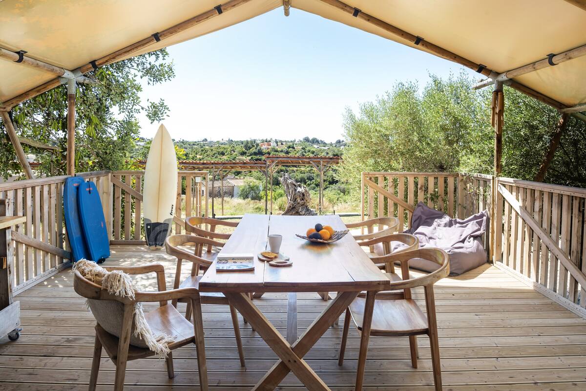 A wooden deck with a table and chairs, a covered area, and a view of the landscape.