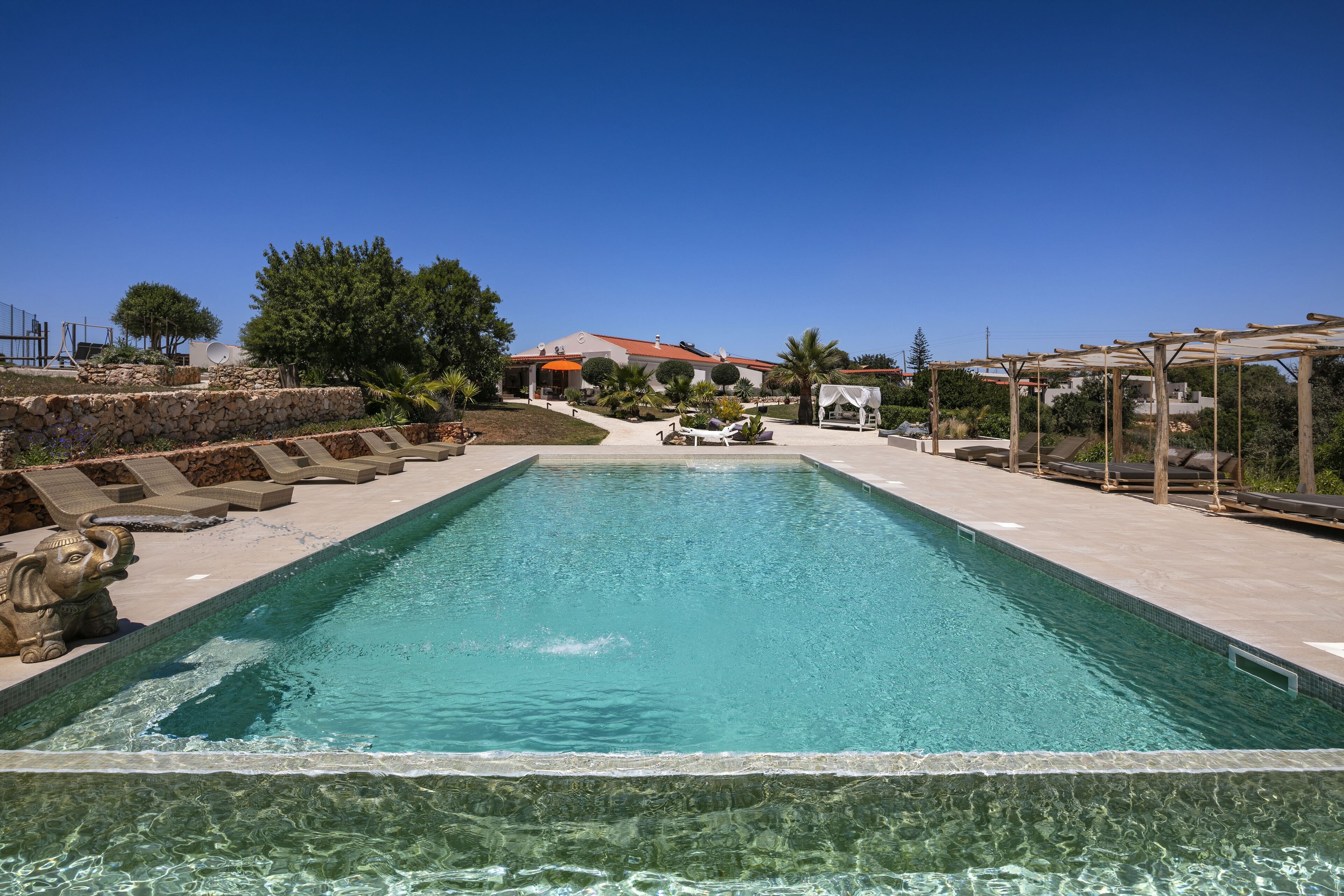 Una piscina rectangular con agua azul cristalina, rodeada de muros de piedra y una estatua de elefante de piedra.
