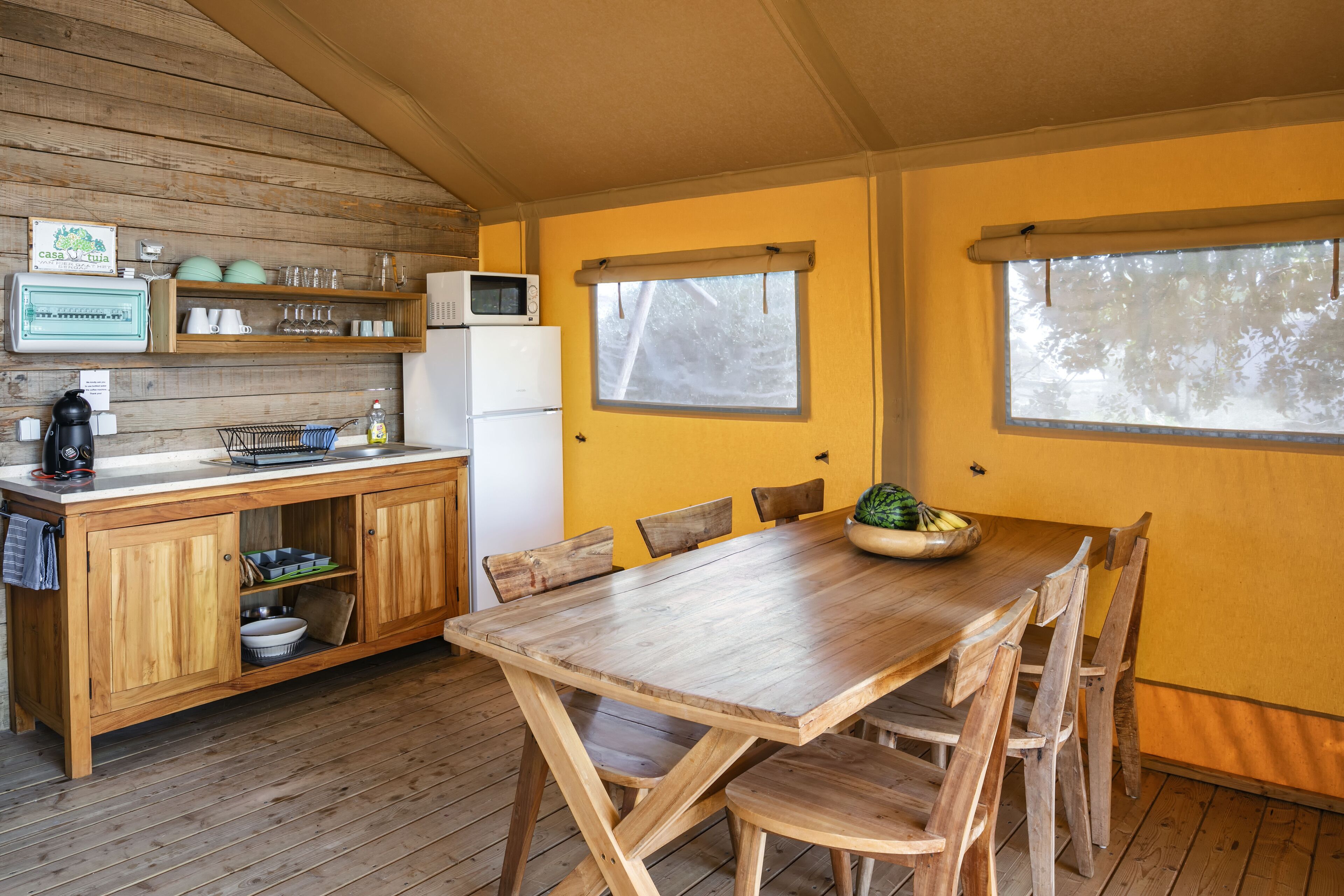 A wooden kitchen with a dining table and chairs, a microwave, and a refrigerator.