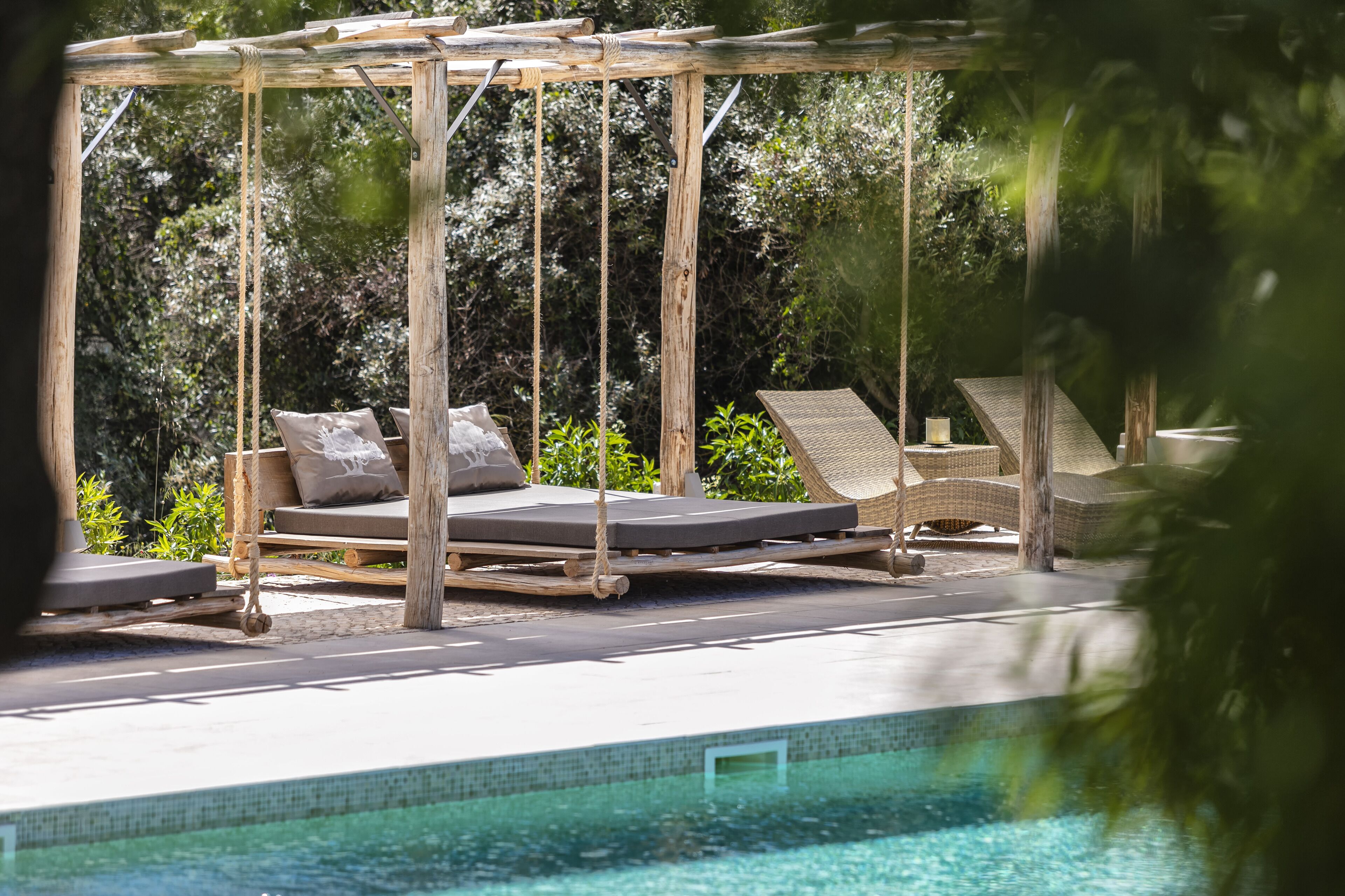 A pool area with a wooden swing chair, a lounge chair, and a cushioned bench.