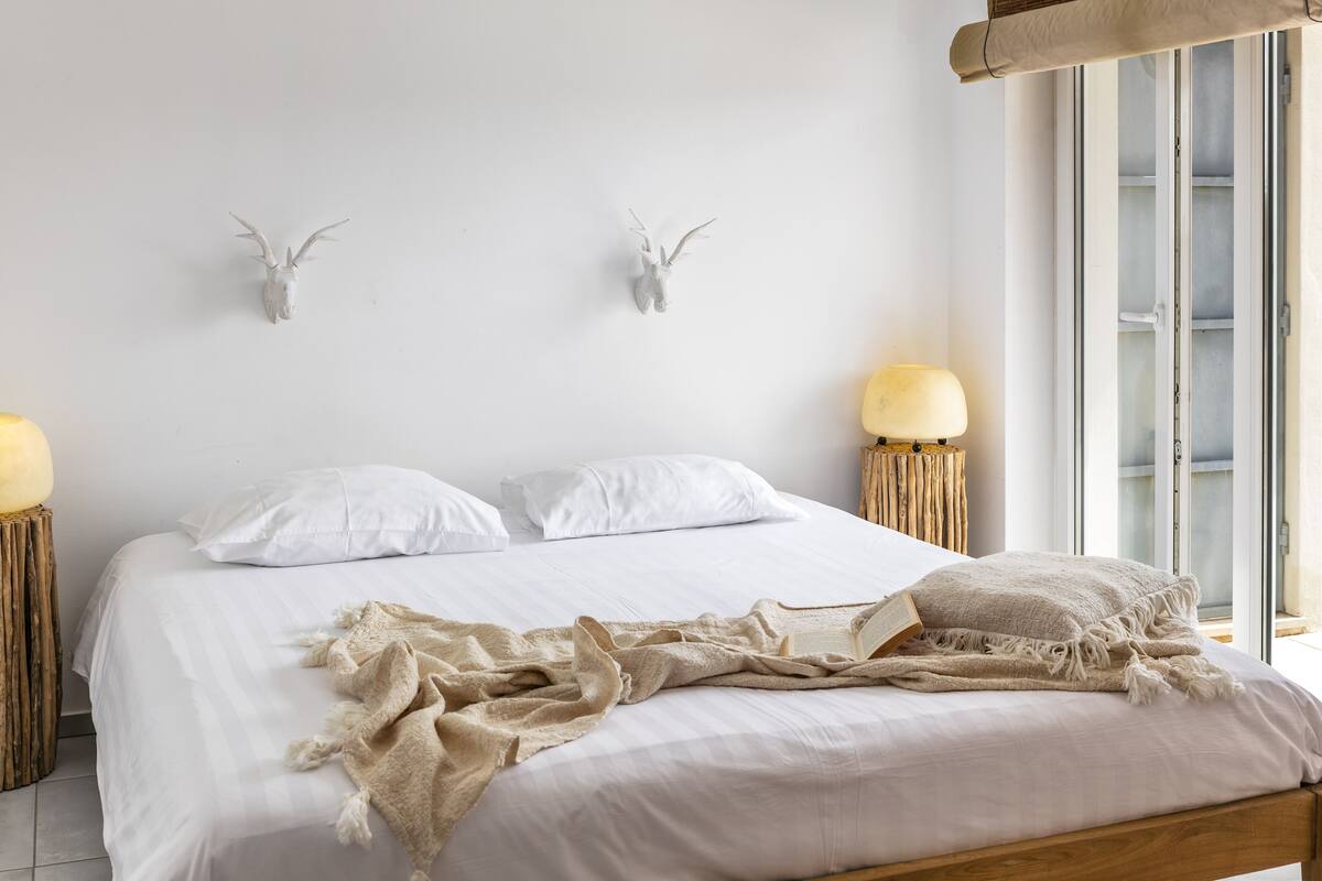 A neatly made bed with white linens and a beige throw blanket, flanked by two wall-mounted animal horns.