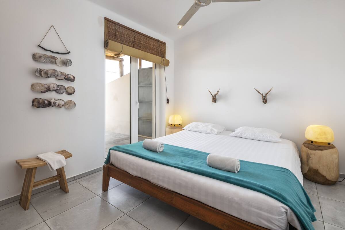 A bedroom with a bed, bedside tables, a bench, a ceiling fan, and wall decorations.