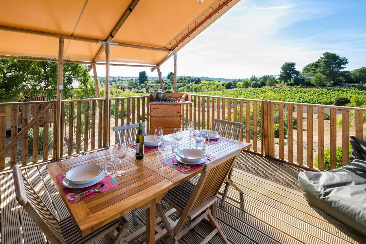 A wooden deck with a table set for dining, overlooking a vineyard.